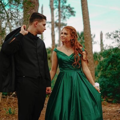 Prom 2019 Dress Ideas from a girl in a long green prom dress with off the shoulder neckline holding hands with date in tux